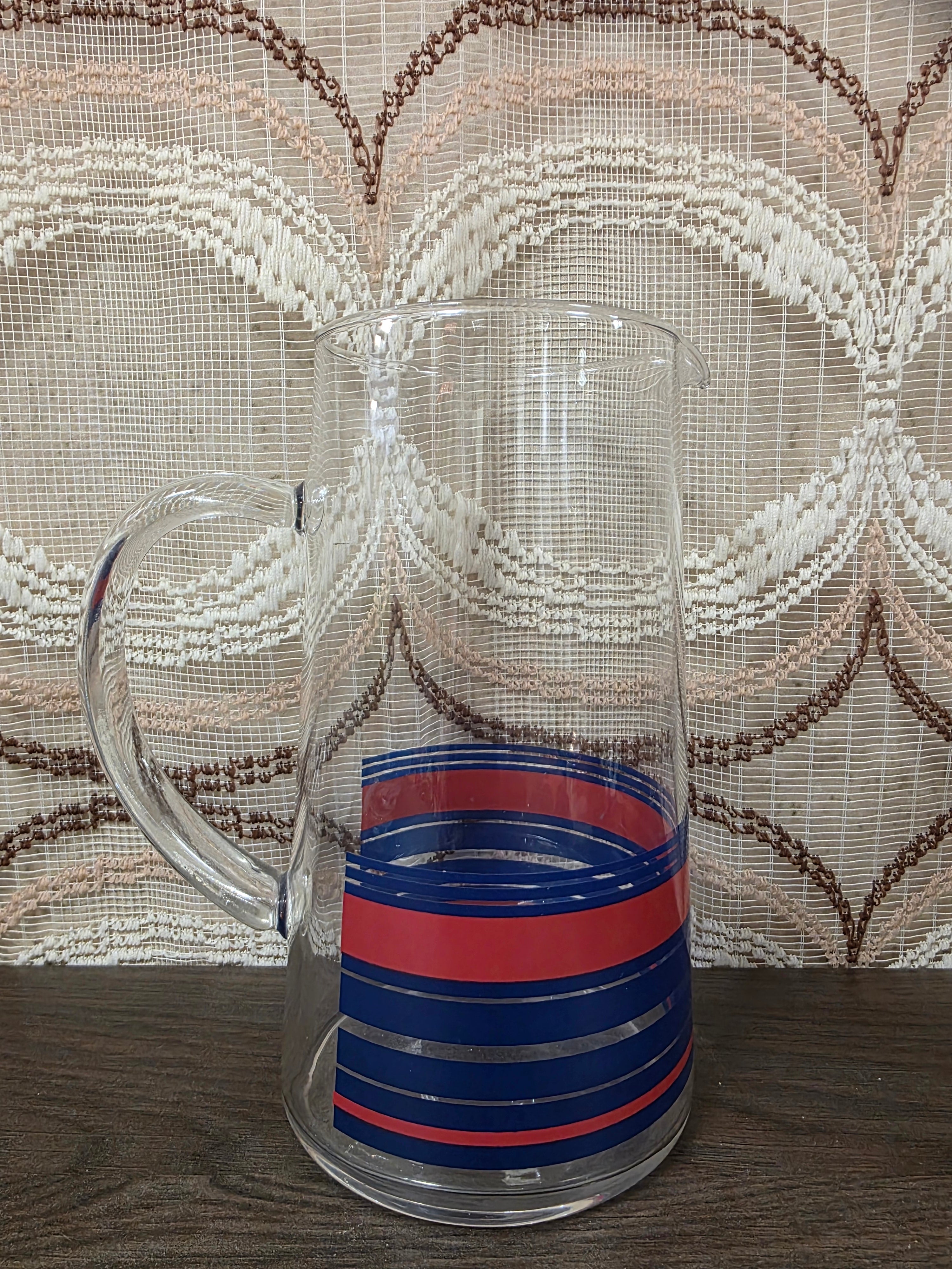 Vintage glazen karaf met rode en blauwe strepen en een glazen handvat.