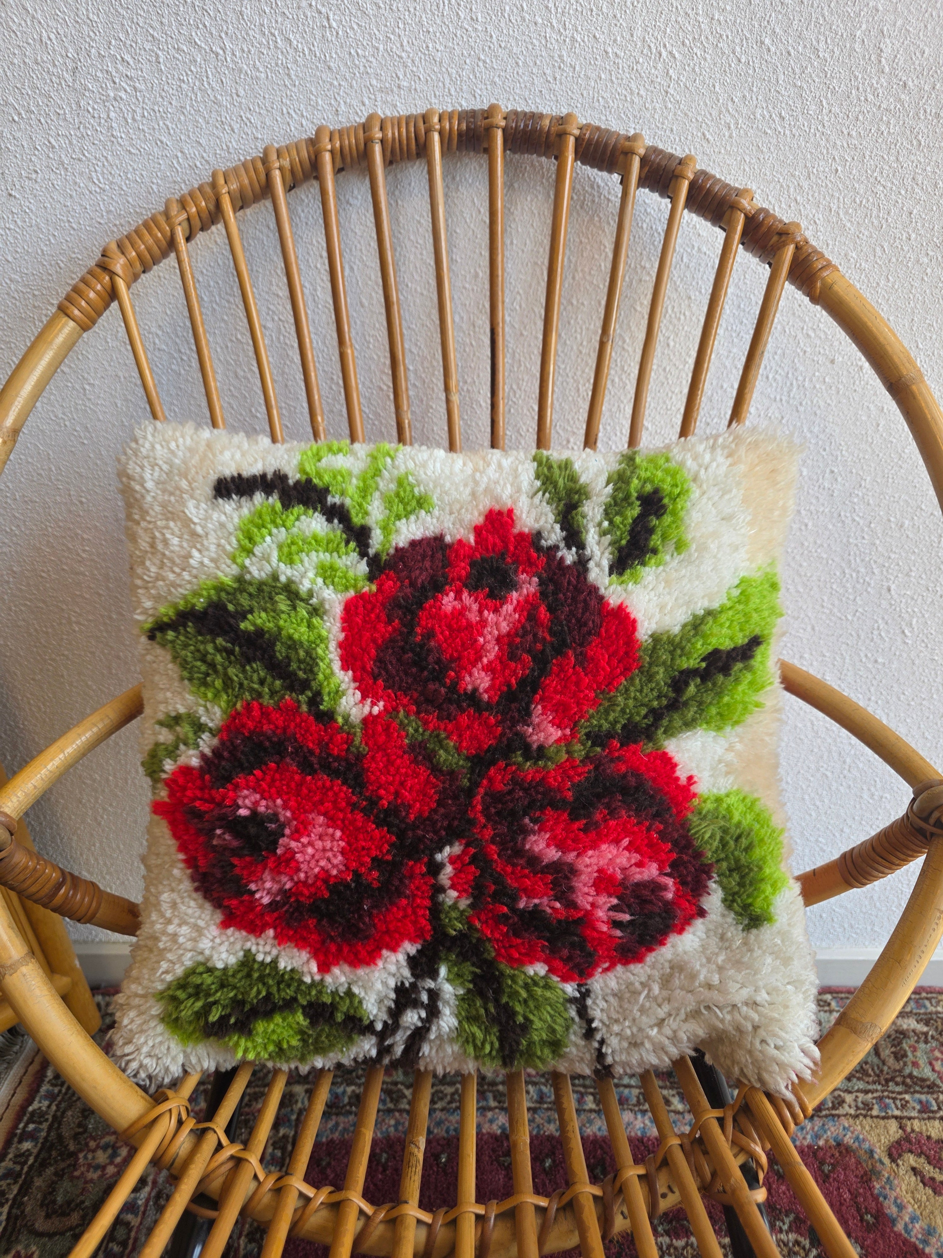 Vintage handgeknoopt bloemenkussen met rode bloemen op een crèmekleurige ondergrond.