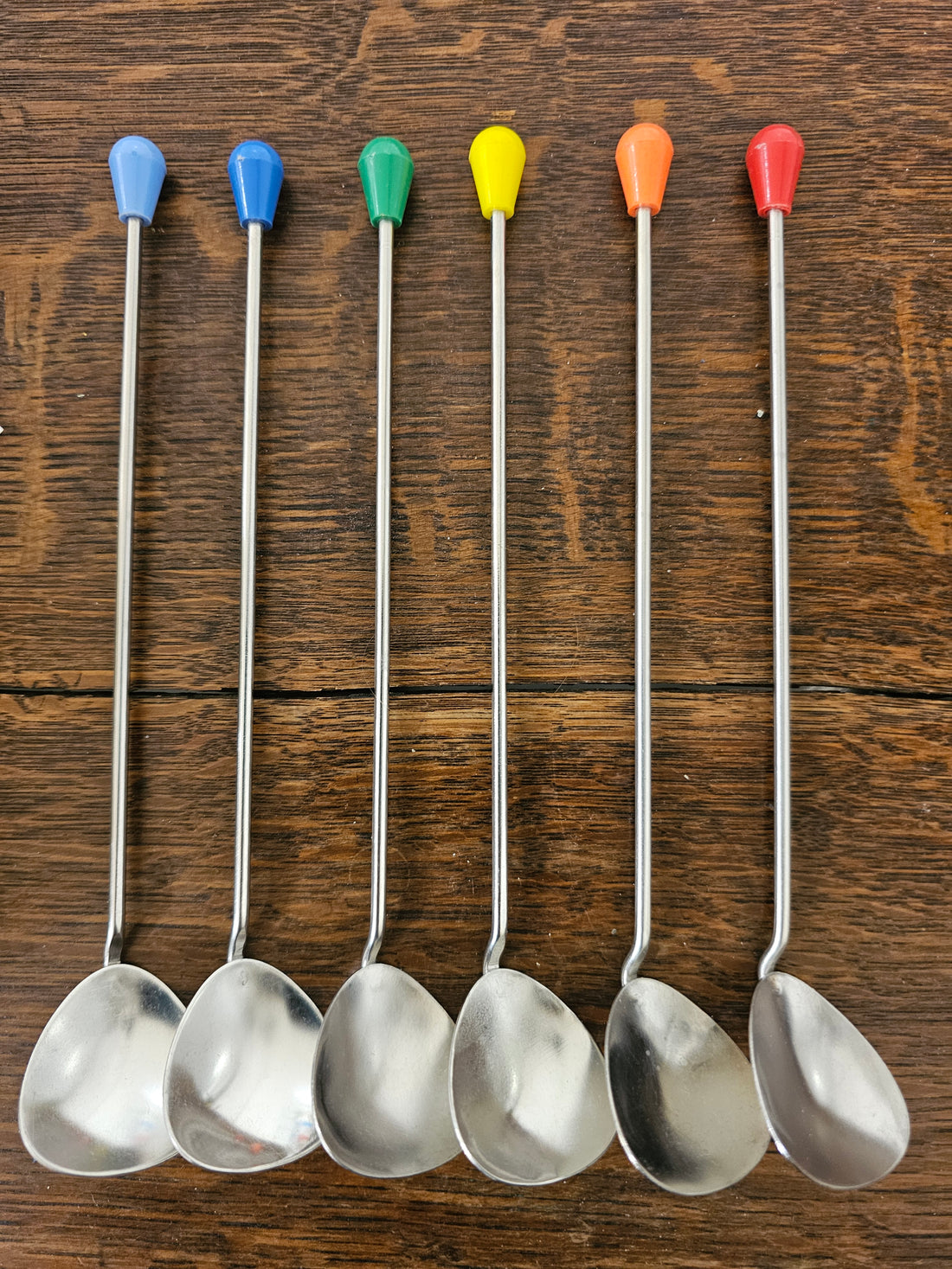 Set van zes vintage sorbetlepels, elk met een eigen kleur aan de bovenzijde, speels gerangschikt.