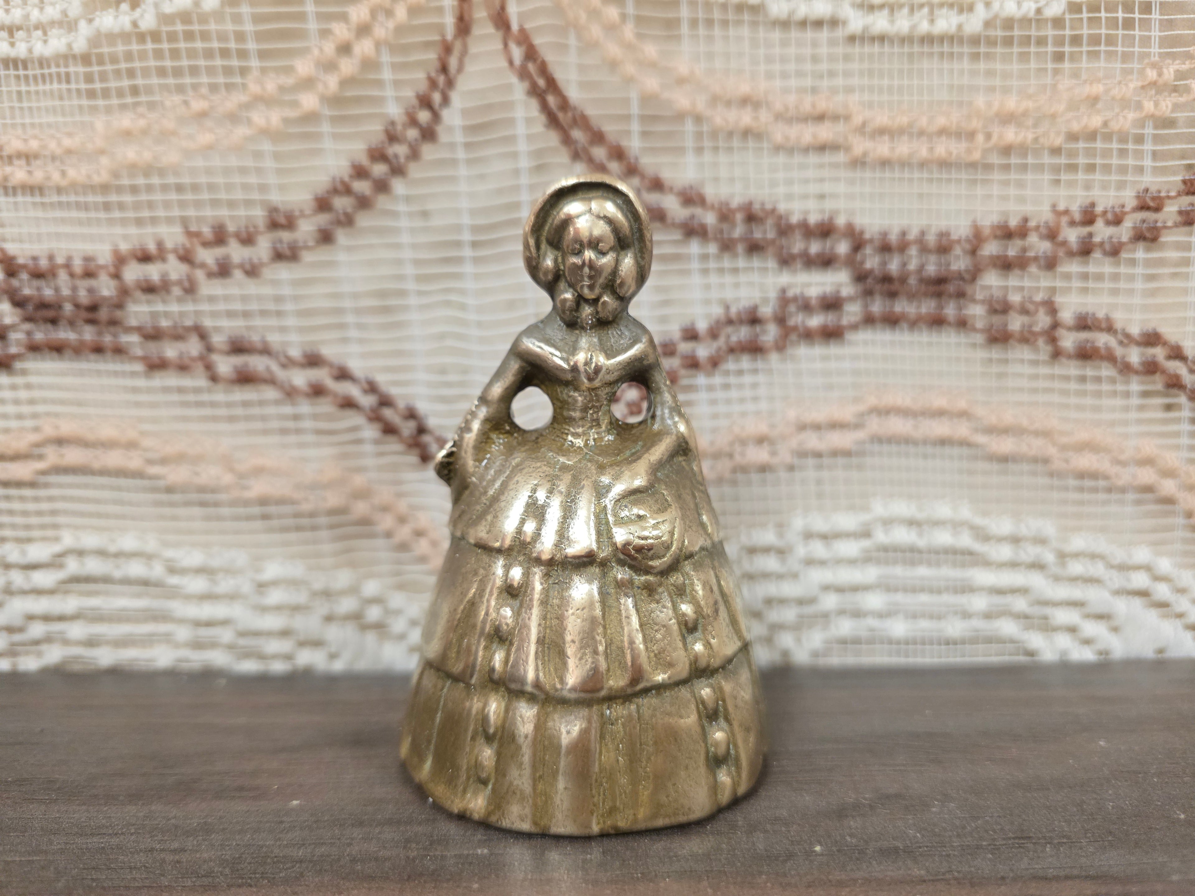 Vintage messing tafelbel in de vorm van een dame met lange jurk en mandje, circa 9 cm hoog.