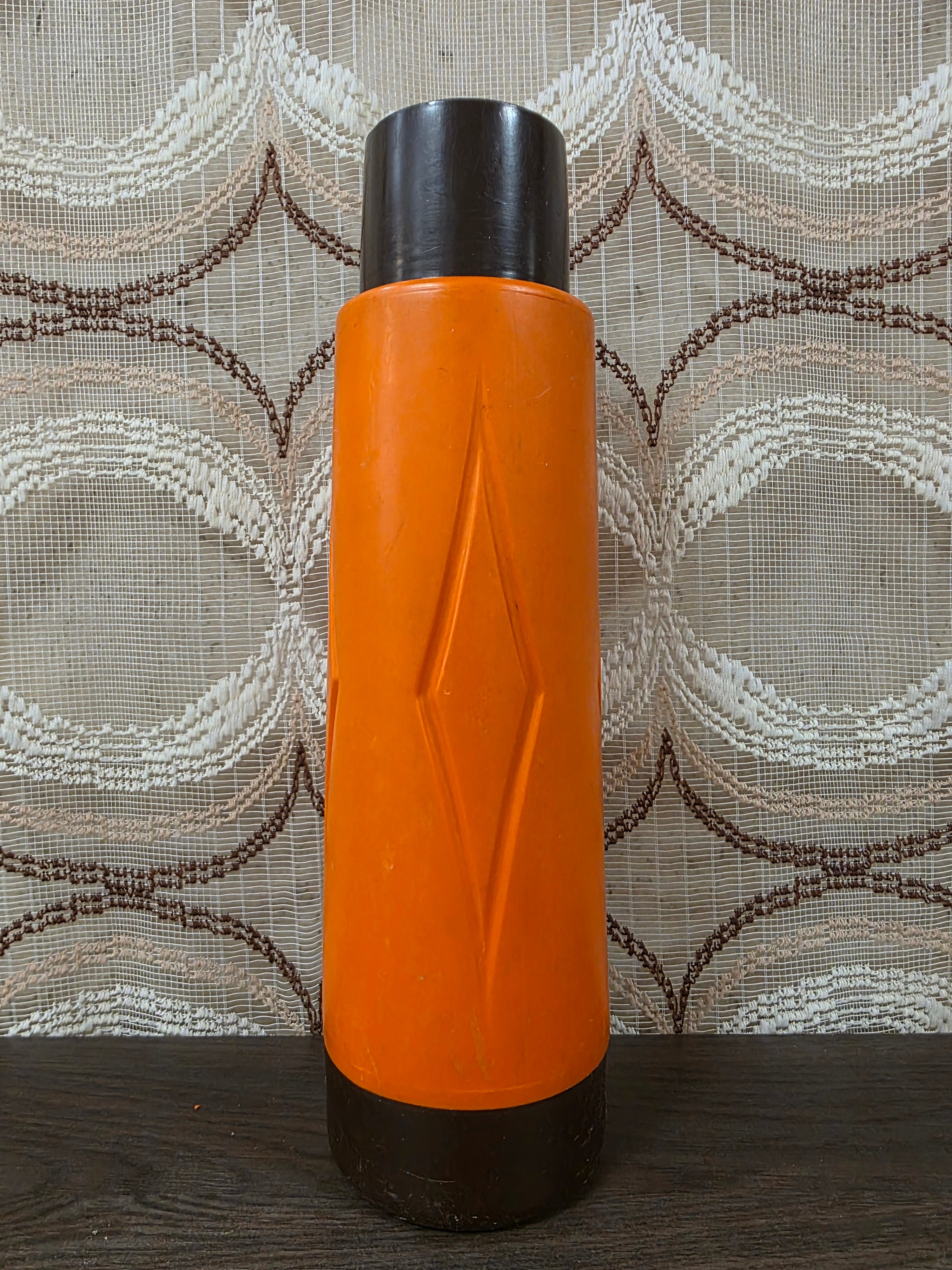 Vintage thermoskan in oranje en donkerbruin kunststof met reliëf aan de voorzijde en een typisch jaren 70 ontwerp.