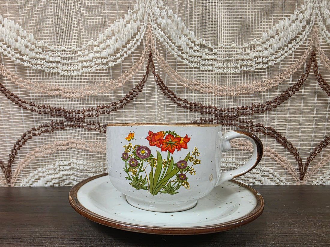 Vintage Wildflower kop en schotel van lichtgekleurd keramiek met subtiele spikkels, bruine rand en een decor van rode en paarse bloemen met kleine veldbloemen.