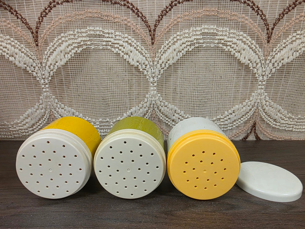 Drie losse Tupperware kruidenpotjes in geel, olijfgroen en crème met hun strooideksels