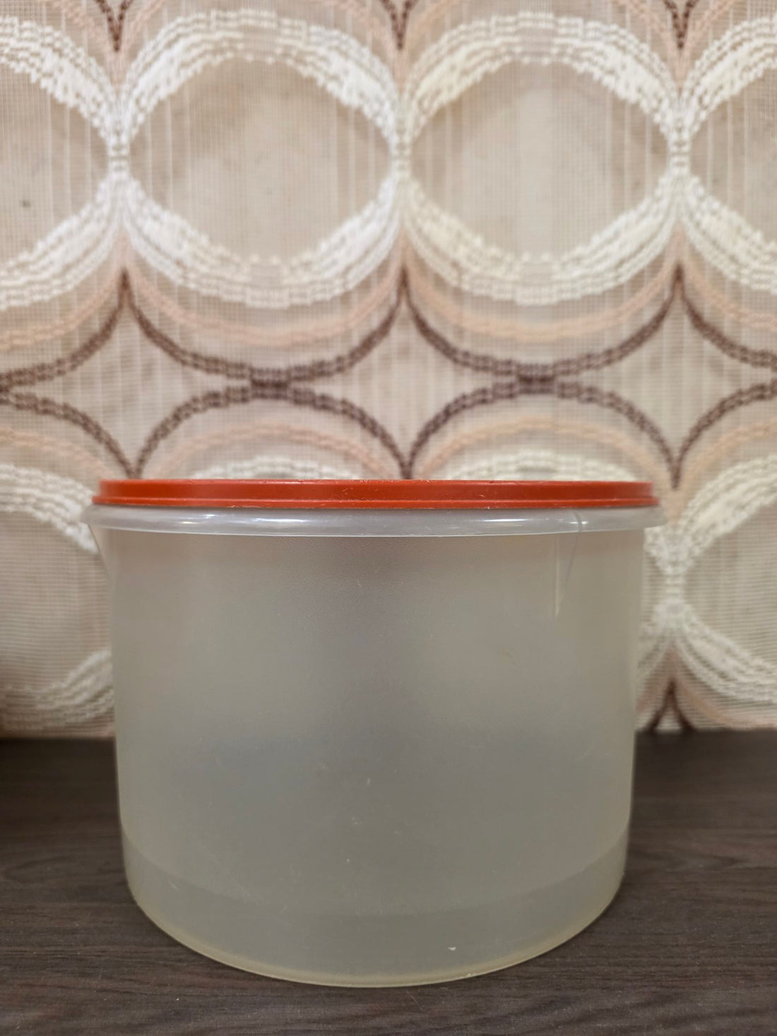 Grote ronde halftransparante Tupperware voorraadbus met oranje deksel, zijaanzicht