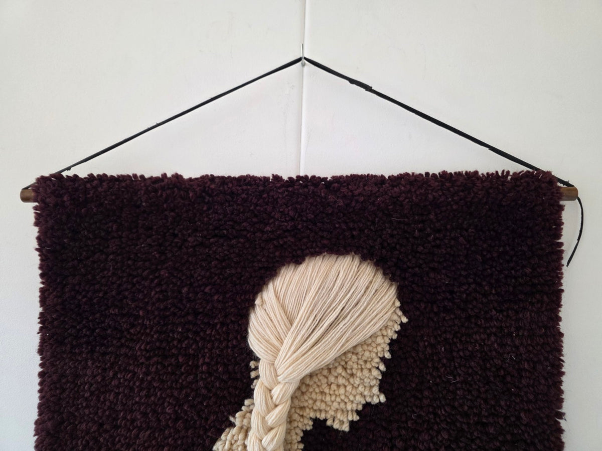 Detail van het crèmekleurige haar en de houten ophangstok van het vintage wandkleed