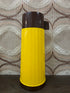 Vintage Aladin thermoskan met geribbelde gele behuizing, bruine dop en originele sticker met lichte gebruikssporen.