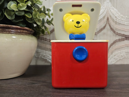 Vintage Ambi Toys Ted in a Box speelgoed – geel beertje in rood doosje met blauwe knop – zichtbare verkleuring aan de randen