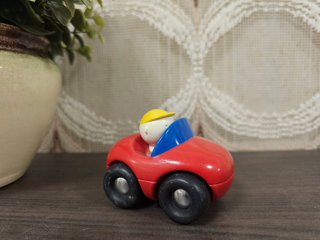 Kleine rode speelgoedauto van Ambi Toys met vrolijk poppetje erin.
