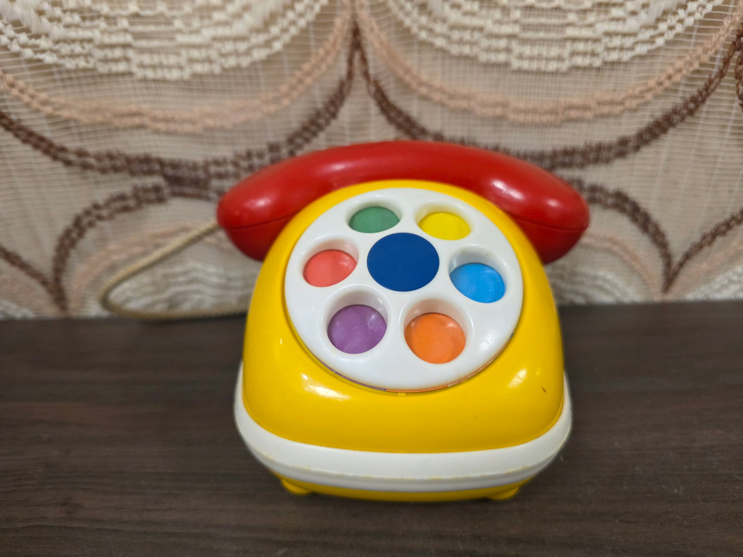 Vintage Ambi Toys speelgoedtelefoon met draaibare draaischijf in geel, rood en wit.