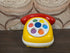 Vintage Ambi Toys speelgoedtelefoon met draaibare draaischijf in geel, rood en wit.