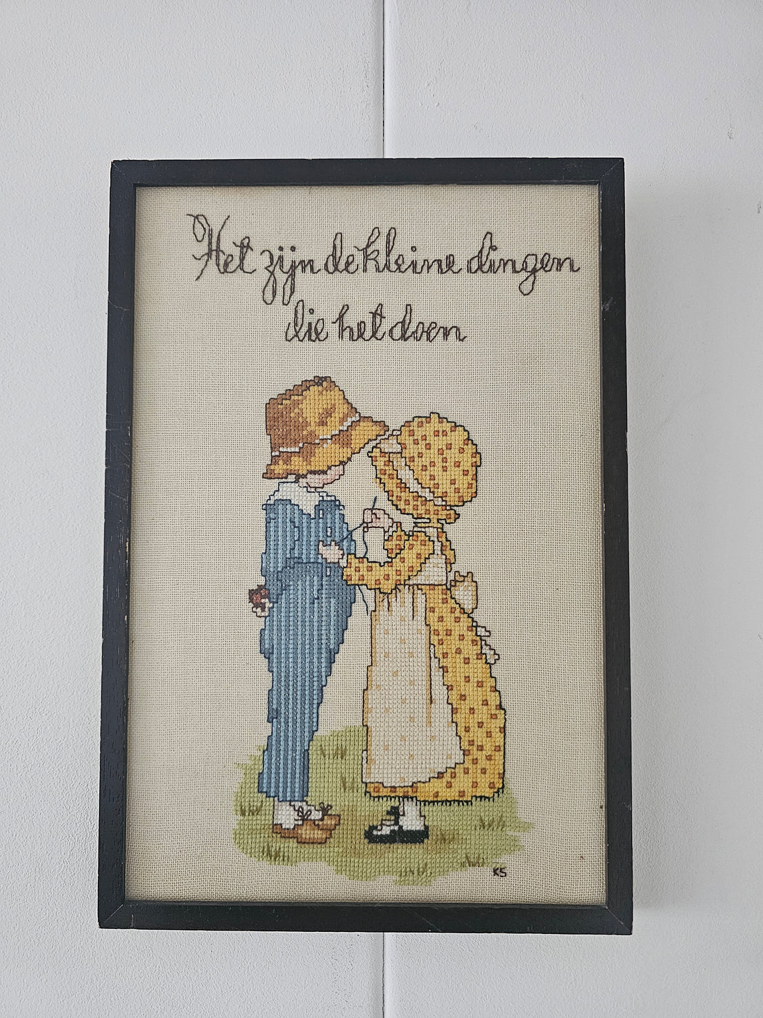 Ingelijst borduurwerk met tekst "Het zijn de kleine dingen die het doen" en afbeelding van meisje en jongen in stijl van Holly Hobbie of Sarah Kay