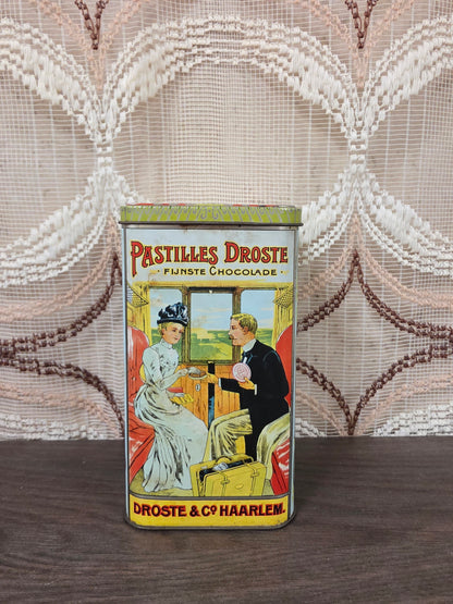 Vintage Droste cacao blik met klassieke reclameafbeeldingen, los deksel en kleurrijke opdruk aan vier zijden