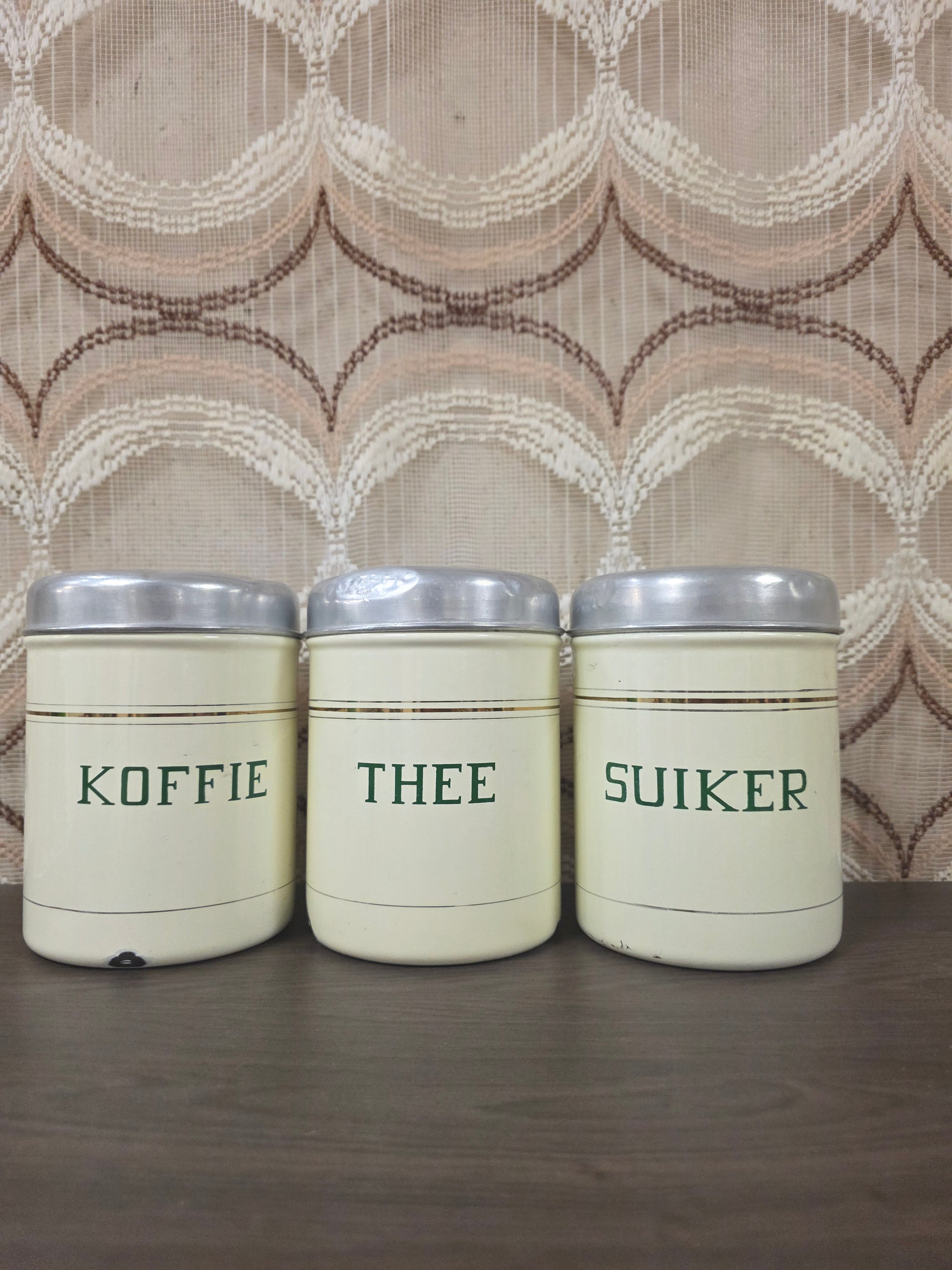 Vintage emaille voorraadbussen voor koffie, thee en suiker met groene opschriften en aluminium deksels.