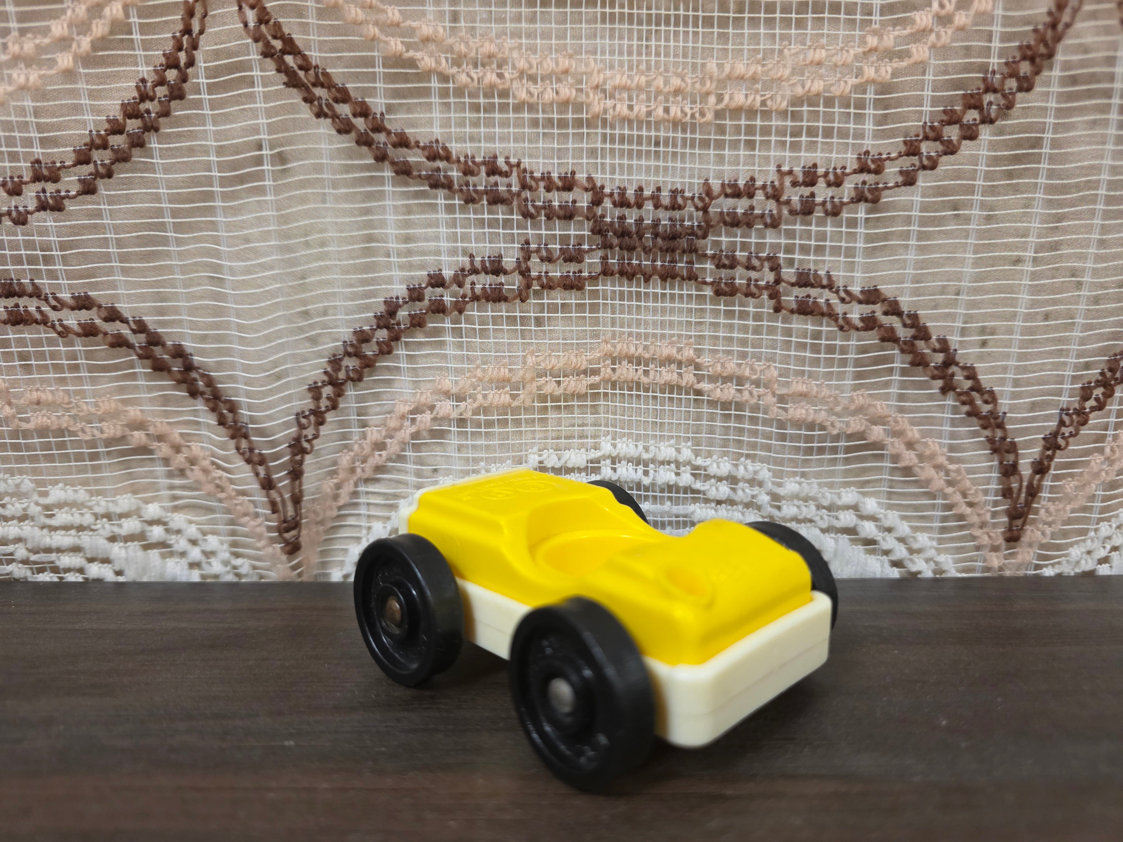 Vintage Fisher-Price autootje in geel wit met zwarte wielen.