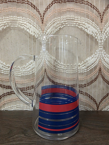 Vintage glazen karaf met rode en blauwe strepen en een glazen handvat.