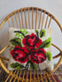 Vintage handgeknoopt bloemenkussen met rode bloemen op een crèmekleurige ondergrond.