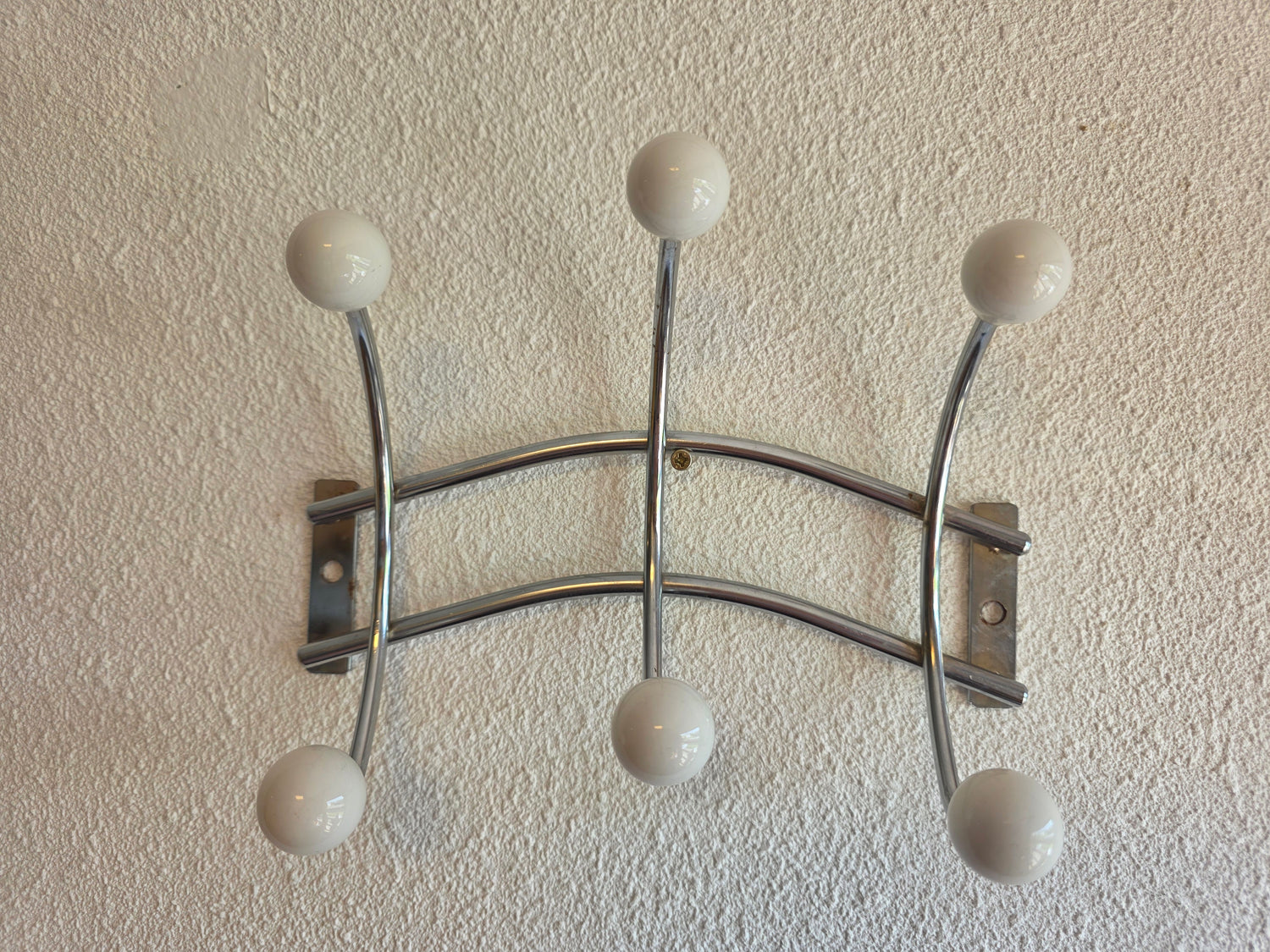 Retro metalen wandkapstok in Sputnik-stijl met zes witte bolknoppen en een zilverkleurig metalen frame van 22,5 cm breed.
