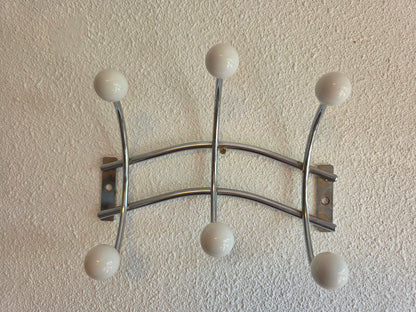 Retro metalen wandkapstok in Sputnik-stijl met zes witte bolknoppen en een zilverkleurig metalen frame van 22,5 cm breed.