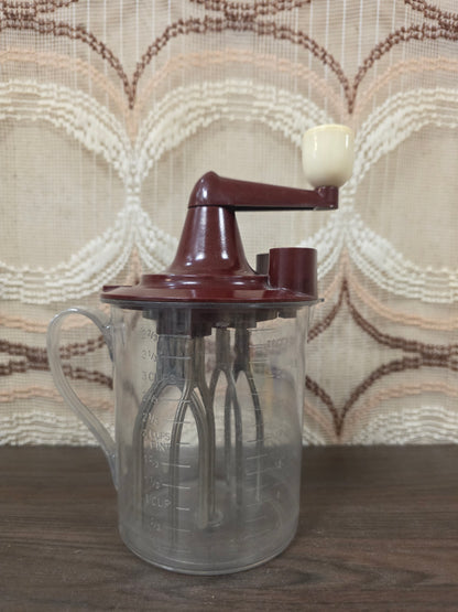 Vintage Maineck handmixer uit de jaren 50 met transparante mengkan en bordeauxrode handzwengel.