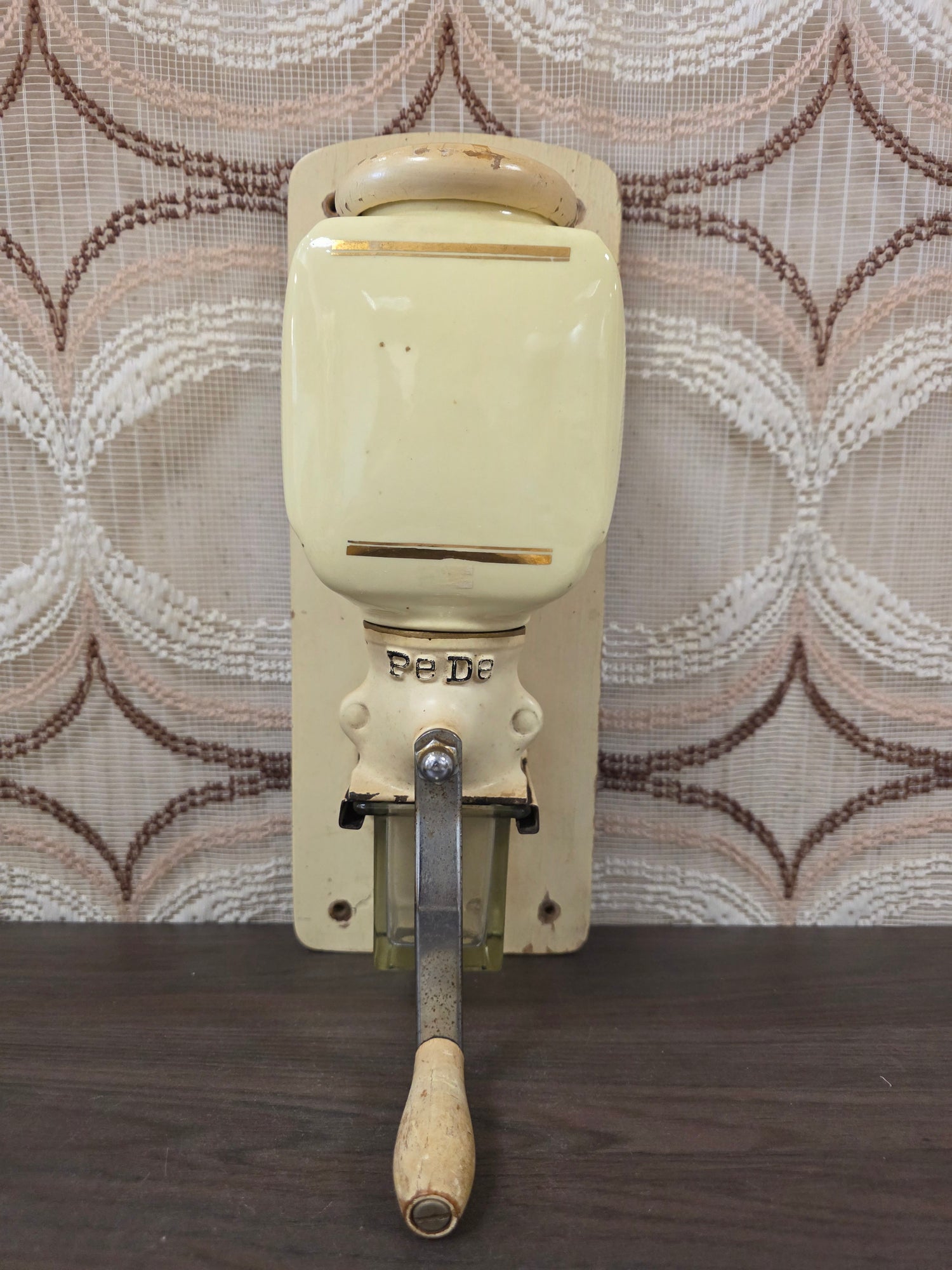 Vintage PeDe wandkoffiemolen in crèmekleur met glazen opvangbakje en houten slingerknop.