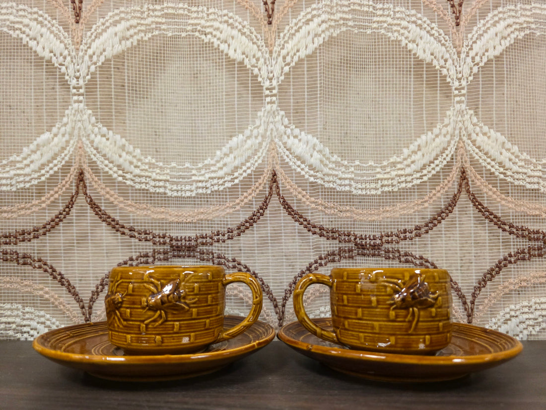 Twee bruine kop en schotel sets met bijenreliëf in aardewerk