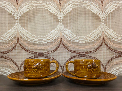 Twee bruine kop en schotel sets met bijenreliëf in aardewerk