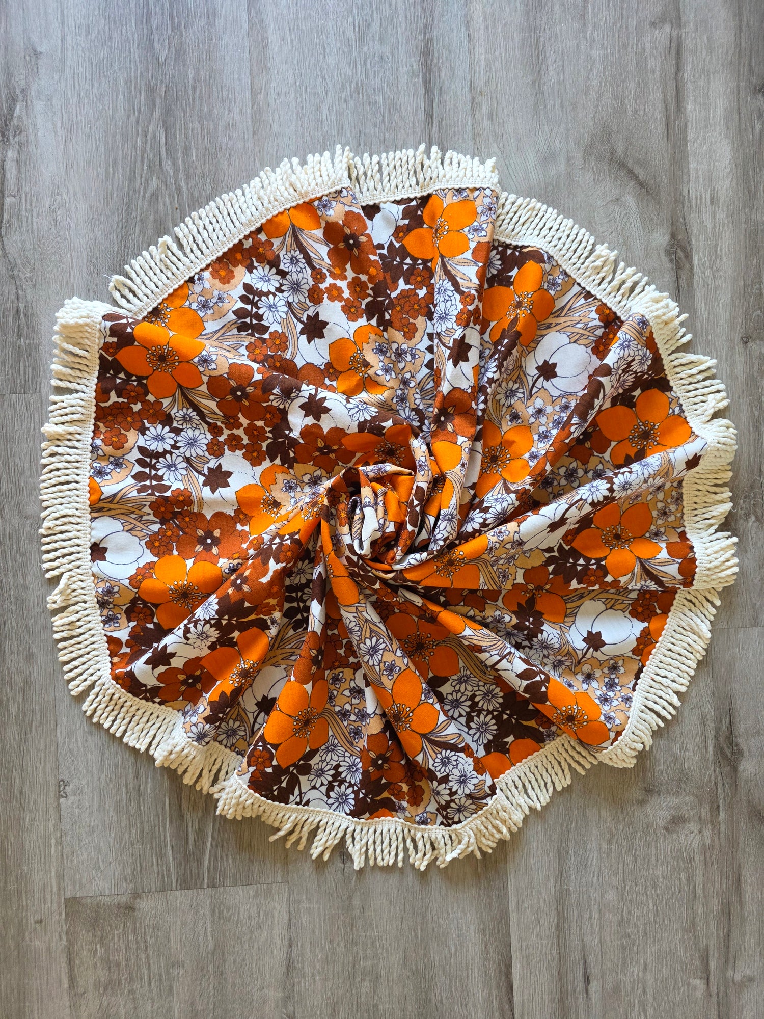 Vintage rond tafelkleed met een bloemenpatroon in oranje en bruintinten, afgewerkt met een crèmekleurige franjerand, diameter 122 cm.