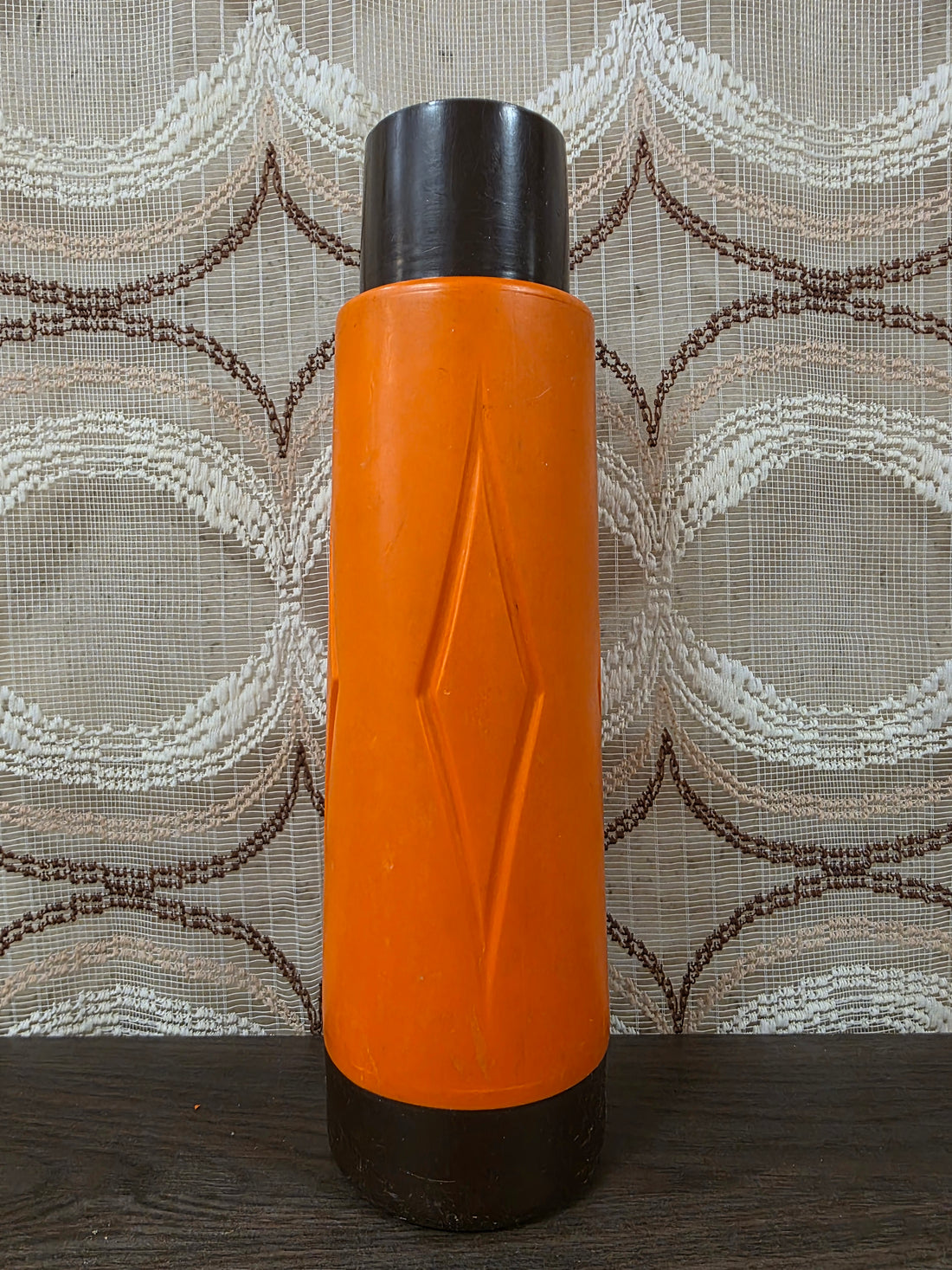 Vintage thermoskan in oranje en donkerbruin kunststof met reliëf aan de voorzijde en een typisch jaren 70 ontwerp.