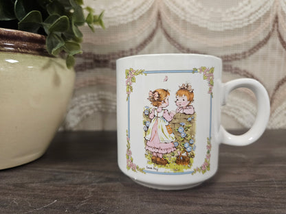 
Vintage Sarah Kay koffiebeker met twee kinderen aan bloemenmuur – wit keramiek
