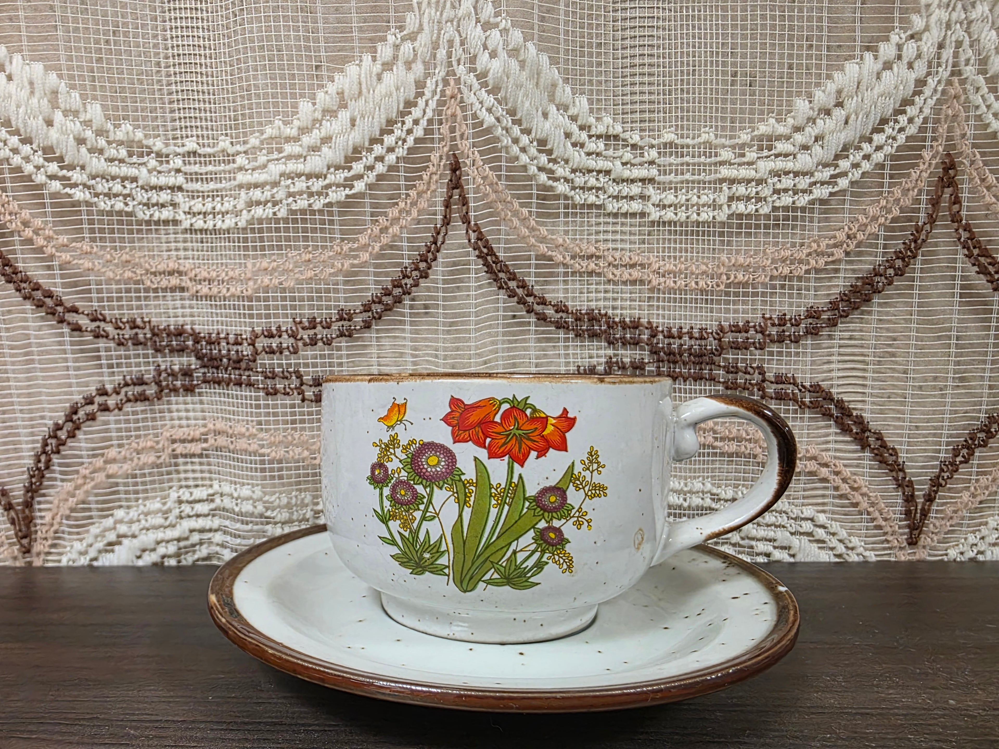 Vintage Wildflower kop en schotel van lichtgekleurd keramiek met subtiele spikkels, bruine rand en een decor van rode en paarse bloemen met kleine veldbloemen.