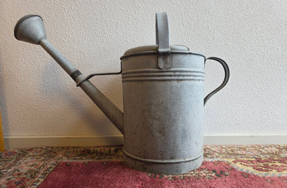 Vintage zinken gieter van 12,5 liter met broeskop en handgreep. De gieter heeft gebruikssporen en een deuk in de zijkant, maar is niet lek.