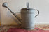 Vintage zinken gieter van 12,5 liter met broeskop en handgreep. De gieter heeft gebruikssporen en een deuk in de zijkant, maar is niet lek.