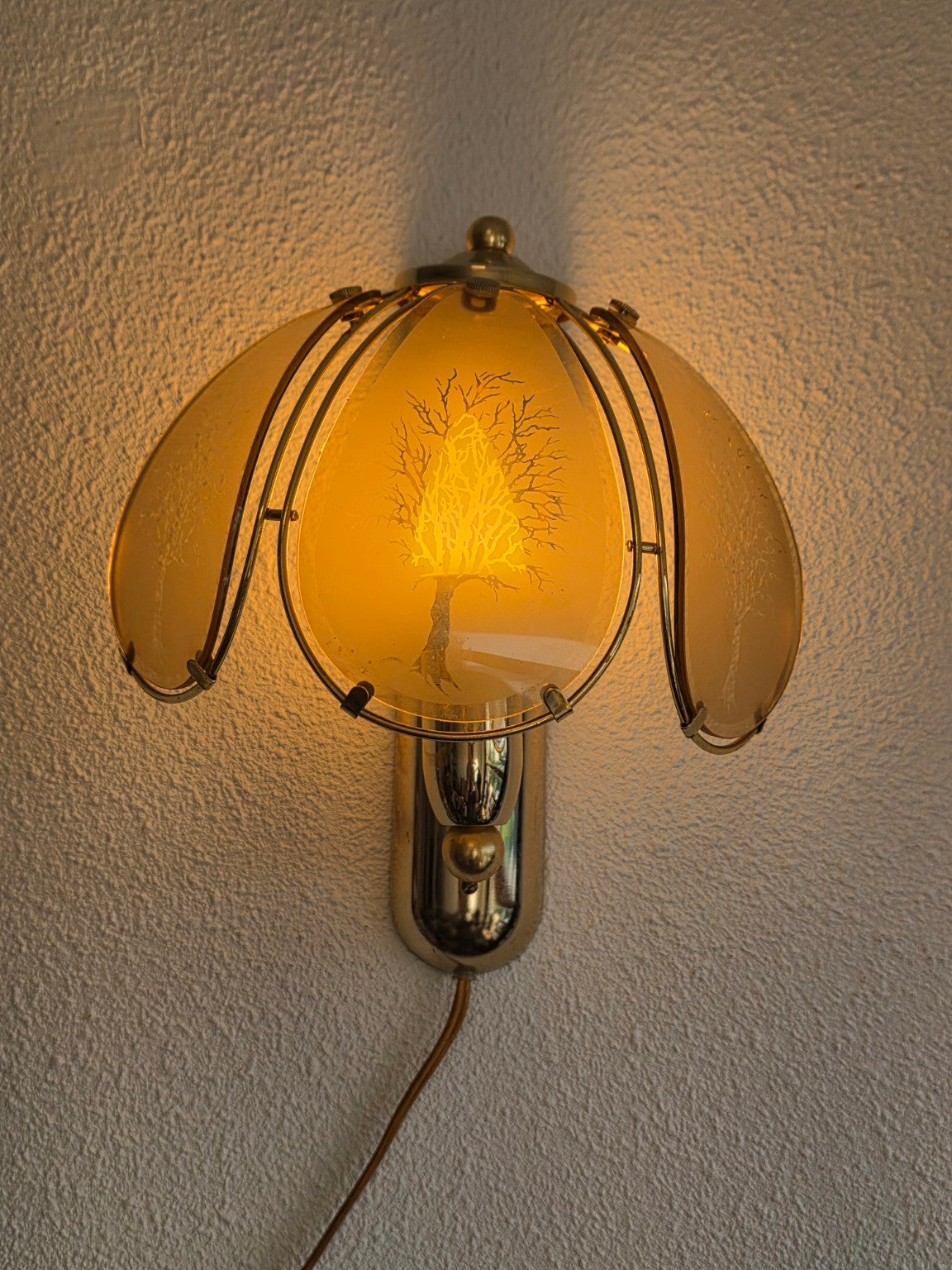 Hollywood Regency wandlamp met rookglazen panelen en boommotief, brandend aan de muur
