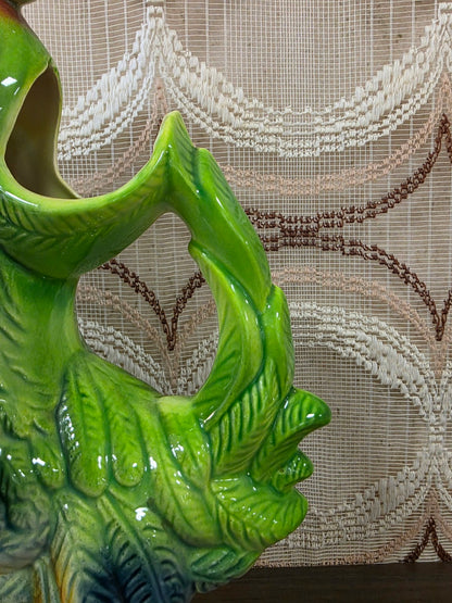 Detail van het groene handvat in de vorm van een hanenstaart en de opening van de schenkkan