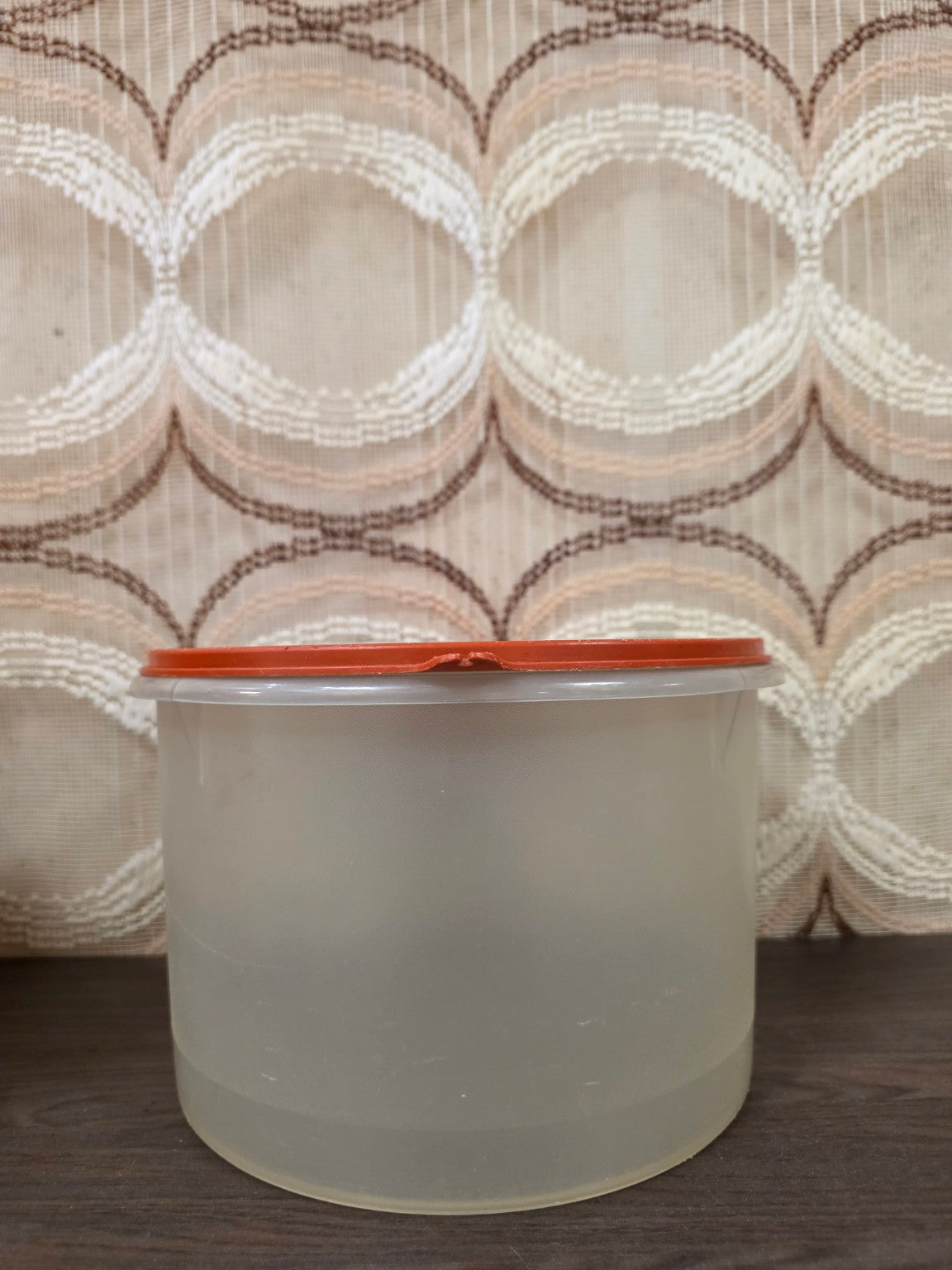 Zijaanzicht van de Tupperware trommel met gebruikssporen aan de rand van het oranje deksel