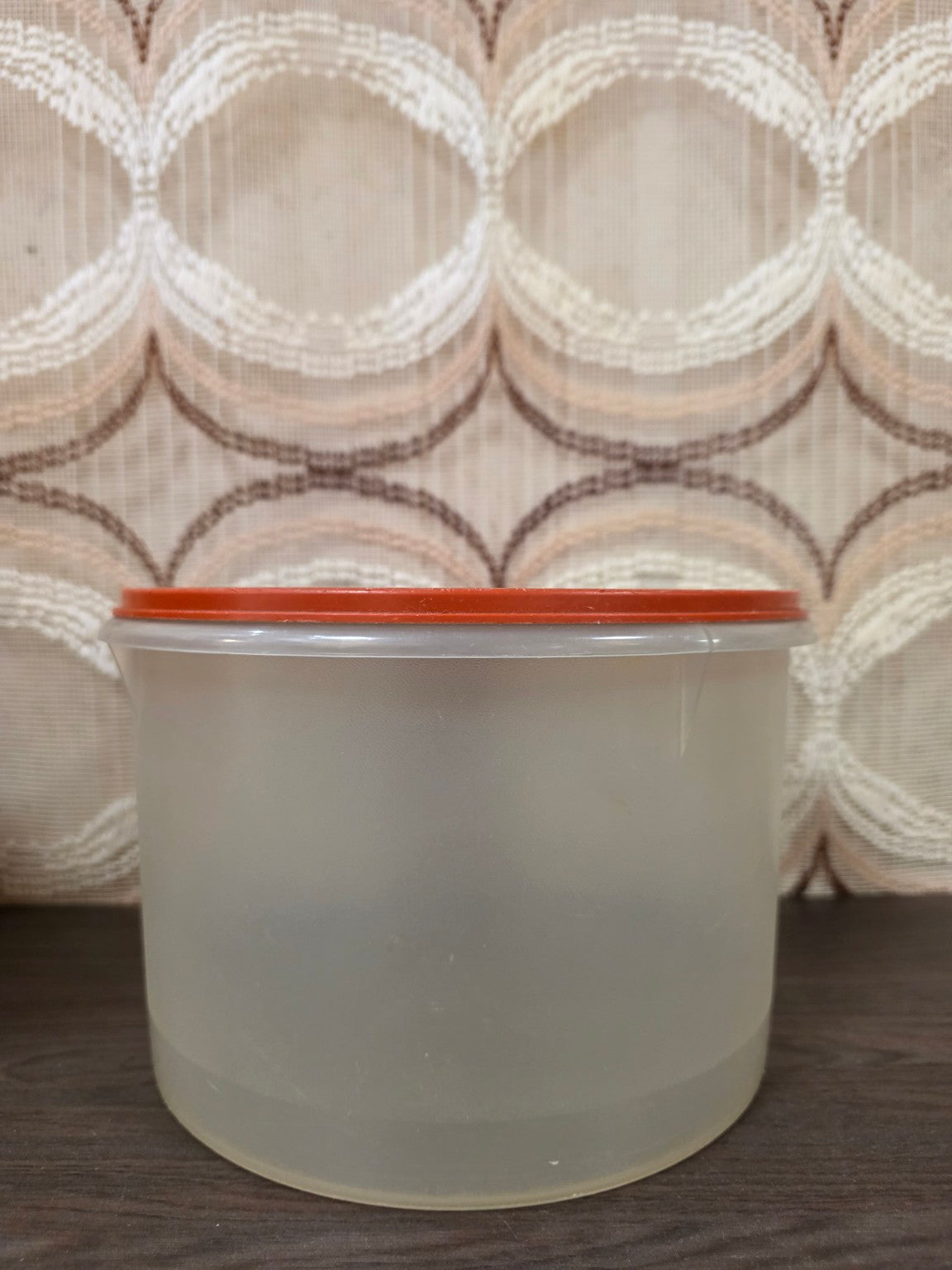 Grote ronde halftransparante Tupperware voorraadbus met oranje deksel, zijaanzicht