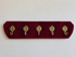 Vintage kapstok met donkerrode corduroy bekleding en vijf messing haken met decoratief gezicht.