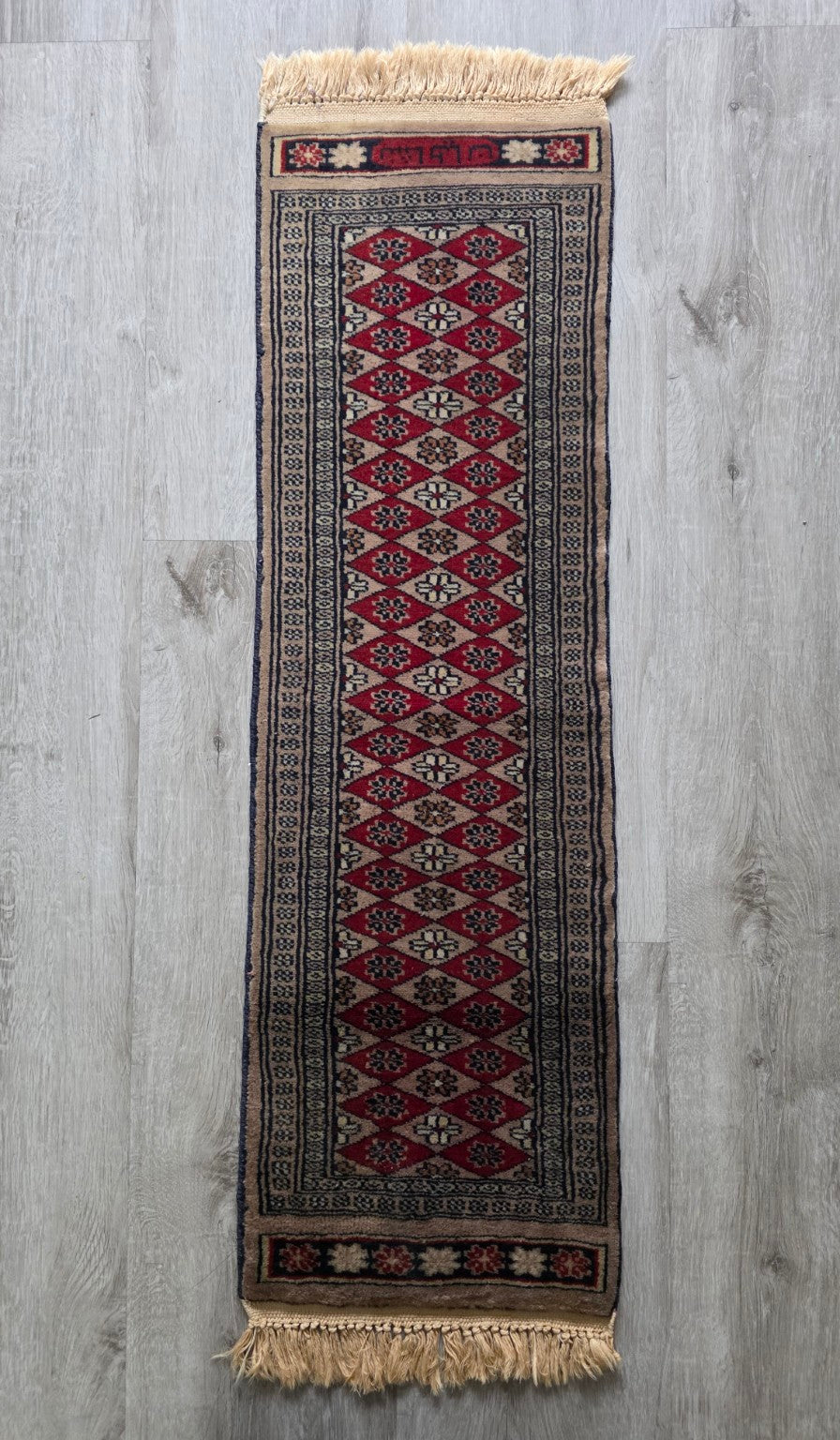 Lange vintage tafelloper met rode ruiten, geometrische motieven in crème, bruin en donkerblauw en franjes aan beide uiteinden.