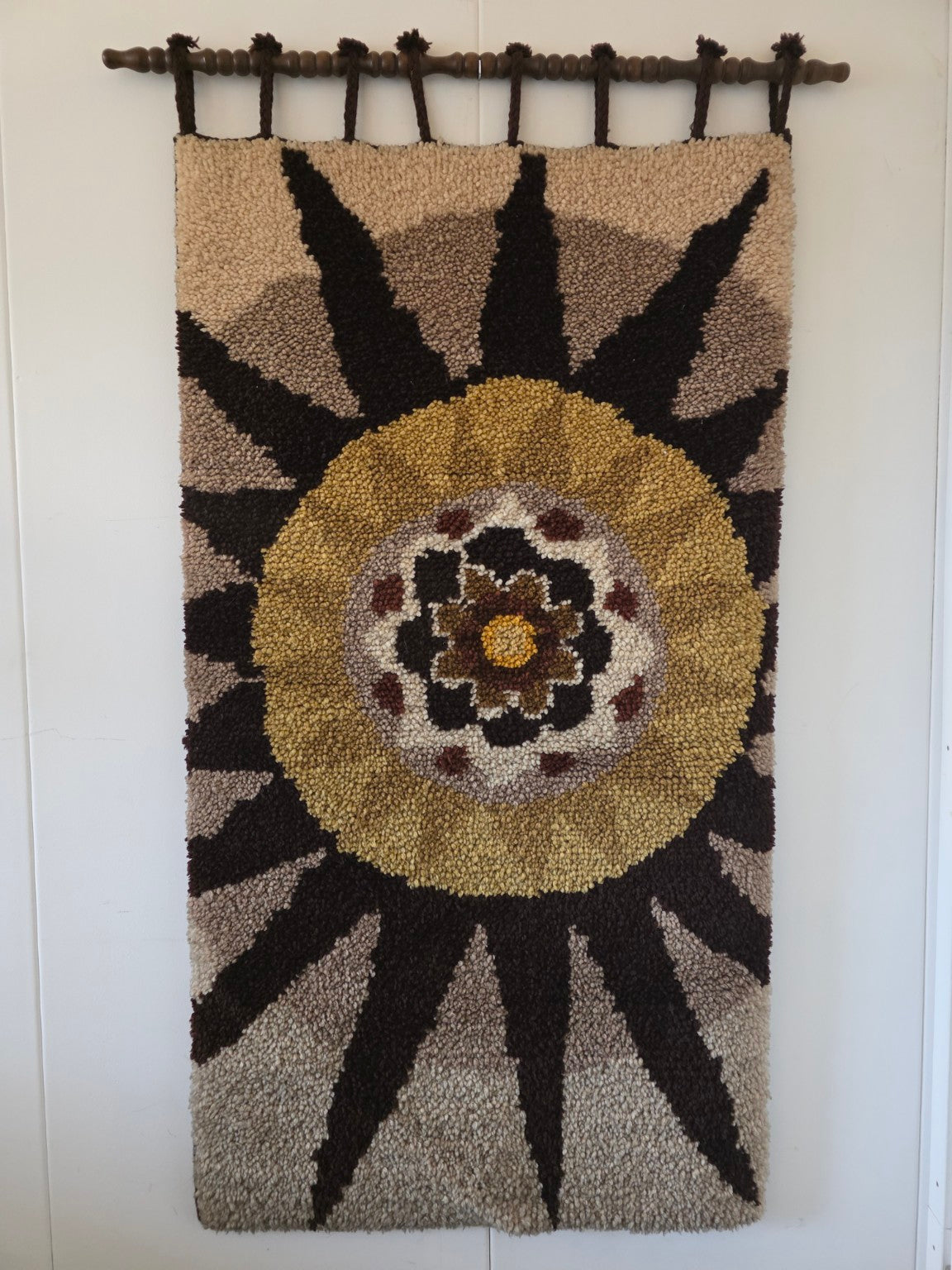 Vintage wandkleed met grote bloem in okergeel, bruin en beige aan een houten ophangstok