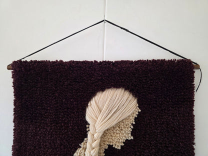 Detail van het crèmekleurige haar en de houten ophangstok van het vintage wandkleed
