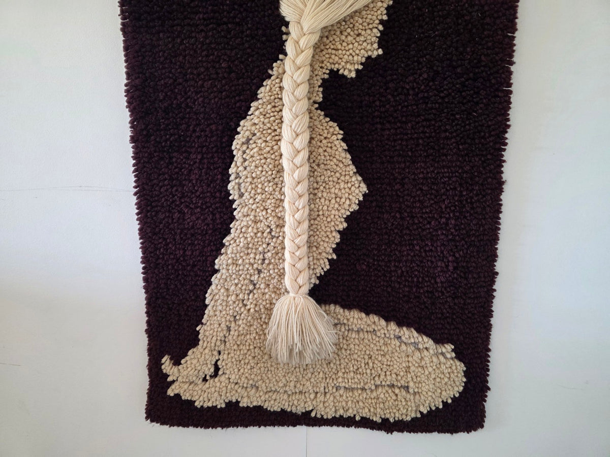 Detail van de zittende vrouw en de onderkant van het geknoopte wandkleed